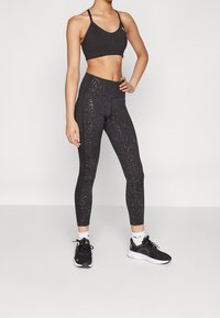 Czarna sportowa biustonosz i legginsy z błyszczącym wzorem, o dopasowanym kroju i elastycznym materiale. W komplecie z czarnymi butami sportowymi.