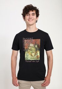 Černé bavlněné tričko s vytištěným uměleckým dílem vázy s květinami, s textem nahoře a dole, zobrazující barvy zelenou, červenou a žlutou.