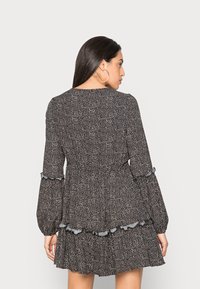 Vestido preto floral com mangas longas, cintura peplum, bainha com volantes e discretos detalhes azuis nas extremidades das mangas. Textura do tecido lisa.