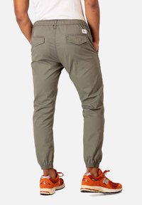 Pantalones jogger verde oliva con cintura elástica, dobladillos ajustados y dos bolsillos traseros. Combinados con zapatillas deportivas naranjas.