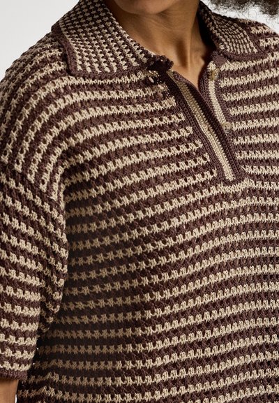 Približnji posnetek osebe, ki nosi rjavo-bež polo majico s kratkimi rokavi iz kvačkanja s črtami in dvema gumboma na ovratniku.