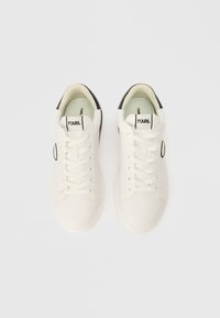 Bijele kožne tenisice s crnim akcentima, okrugli nos, ravni potplat i tradicionalno vezanje sprijeda. Brendiranje "KARL" na jeziku.