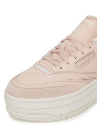 Rózsaszín tornacipő, velúr és sima bőr felsőrésszel, mintás gumitalppal és Reebok márkajelzéssel az oldalán és a nyelvén.