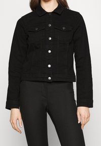 Musta farkkutakki, jossa on kauluskrae, kaksi rintataskua, hopeiset napit ja lyhennetty muoto. Sujuva tekstuuri ja tiukat hihat.