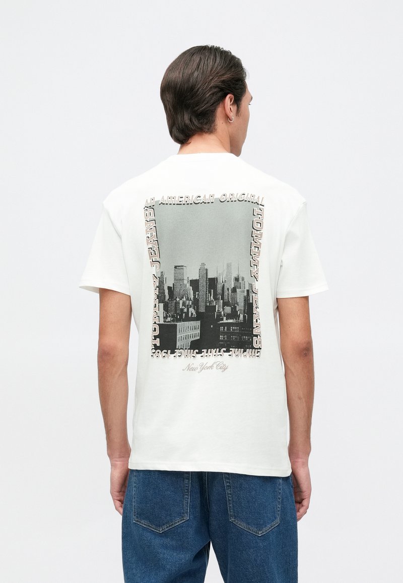 Camiseta de algodón blanca con un gráfico de paisaje urbano en blanco y negro en la parte posterior, enmarcado por texto en diferentes tipos de letra. Mangas cortas y corte relajado.