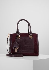 Krokodillemønstret bordeaux håndtaske med guld hardware, dobbelte håndtag, aftagelig skulderrem og dekorativ kvast.
