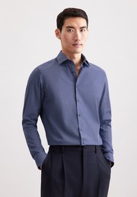 Camicia a righe blu navy con punti bianchi, colletto abbottonato, maniche lunghe, abbinata a pantaloni scuri, che presenta un design aderente.