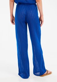Blauwe, gemusterde, doorschijnende wijde broek met een gestructureerd ruitpatroon, voorzien van een elastische tailleband en een iets losvallende pasvorm.