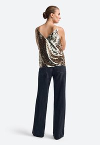 Kuld- ja hõbedase sädelusega tank-top V-nupo disainiga, kantud kõrge vöökohaga tume denimpüksid, millel on laienev lõige. Sile tekstuur, ilma varrukateta stiil.