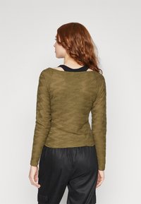 Tricou lung cu maneci în verde măsliniu, cu un design texturat și pliat, decolteu rotund și umeri ușor gathered. Top negru pe dedesubt.