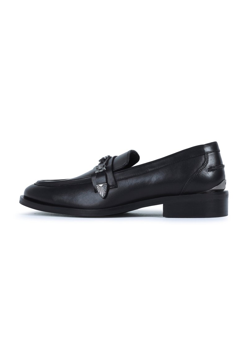 Mocasines de cuero negro con una punta redondeada y un tacón bajo de bloque. Presentan herrajes metálicos decorativos en la parte superior. Textura suave.