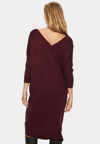 Robe en maille bordeaux avec un dos en V profond et des manches trois-quarts. Coupe ample et tissu texturé avec un design simple.