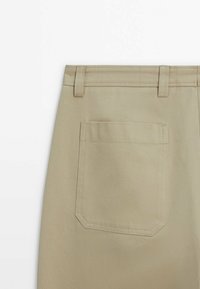 Back of beige pants showing belt loops and a single patch pocket stitched on the right side.