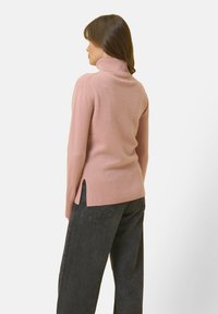 Jasnoróżowy sweter z golfem wykonany z miękkiego materiału. Posiada ribbowe mankiety i dół, z bocznymi rozporkami dla wygody. Nosi się go z ciemnymi dżinsami.