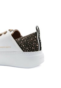 Weißer Sneaker mit erhöhtem Profil, braunen Schnürsenkeln und einem schwarzen, genoppten Rücken mit metallischen Akzenten. Mit der Marke "ALEXANDER SMITH" versehen.