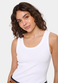 Valge ribadega tank top, millel on ümar kaelus, kehasümpaatne lõige ja laiad õlavarrerihmad. Sile tekstuur, ilma nähtavate mustrite või aksessuaarideta.