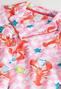 Rosa Pyjama-Set mit einem Hummer-Druck auf einem Schachbrett-Hintergrund, ergänzt durch grüne und blaue Sterne sowie weiße Akzente. Weiche Stoffstruktur.
