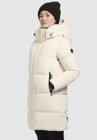 Parka blanche gonflée avec capuche, présente des poches latérales zippées, des accents noirs contrastants et une finition lisse et texturée.