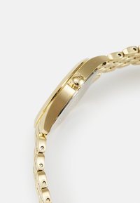 Montre en métal doré avec un boîtier lisse et poli, un cadran rond, et un bracelet à maillons comprenant des connecteurs ronds et une couronne latérale pour les ajustements.