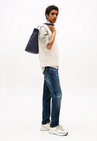 Biały dziany bezrękawnik na zielonej koszuli w kratę, niebieskie dżinsy i szare trampki. Na ramieniu zawieszona jest ciemnoniebieska torba.