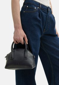 Zwarte gestructureerde leren handtas met twee korte handvatten. Compacte, ronde vorm met ritssluiting en subtiele logo-detail aan de voorkant.