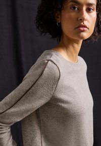 Lichtbeige trui met een gestructureerde brei, ronde halslijn en contrasterende bruine stiksels langs de schouderna seams.