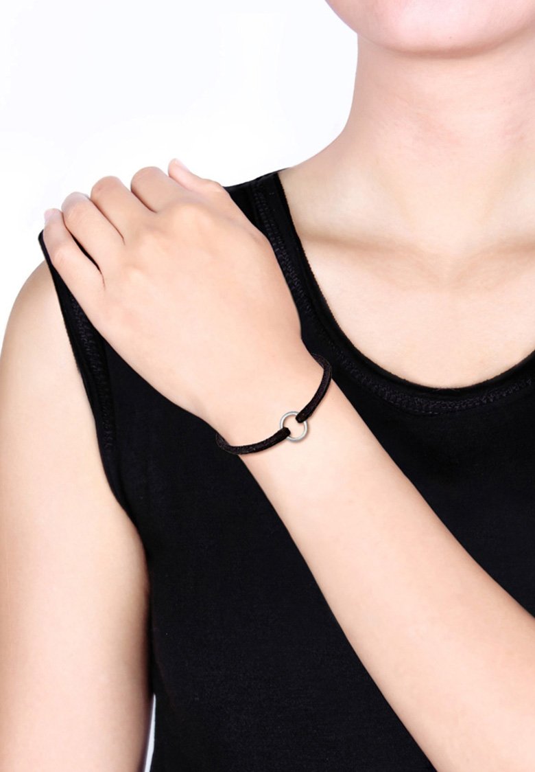 Svart snoddarmband med en silverfärgad rund spänne, bärs på ett handled, med en slät, minimalistisk design mot en mörk skjorta.