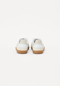 Hvite sneakers med et lyst beige semsket aksent, gummisåle, avrundet design, og polstret krage, som viser minimalistisk bakmerke.