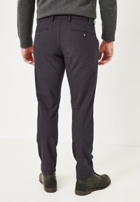 Dunkelgraue Hose mit schmaler Passform, zwei Gesäßtaschen und Knopfdetails. Kombiniert mit dunklen Schuhen, die eine glatte Stoffstruktur zeigen.