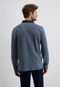Marineblaues Langarm-Polo mit einem strukturierten Muster und kontrastierendem Kragen. Verfügt über einen geraden Saum und weichen Stoff für zusätzlichen Komfort.