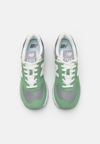 Baskets vertes et grises avec une tige en mesh et en daim, lacets blancs et semelle en caoutchouc grise ; présente le logo New Balance et le numéro de modèle 574.