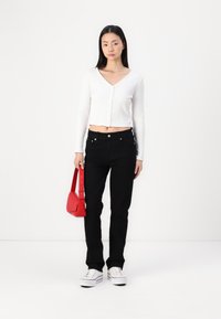 Λευκό ριμπ cropped μπλουζάκι με μακριά μανίκια, ψηλόμεσα μαύρα τζιν, κόκκινη τσάντα και λευκά Sneakers, σε απλό φόντο.