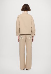 Beige cropped jacket with a collar, paired with wide-leg beige trousers featuring floral embroidery and lace detailing on pockets.