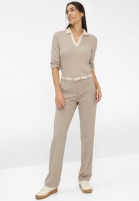 Beige gestreiftes Langarmoberteil mit V-Ausschnitt und cremigem Kragen, kombiniert mit beigen, taillierten Hosen und hellen Sneakers.
