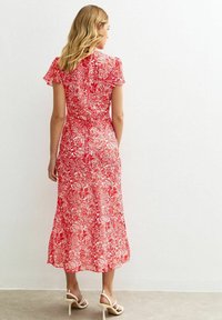 Robe midi fleurie rouge avec des manches courtes à volants, arborant un motif botanique, taille cintrée et ourlet évasé. Texture de tissu lisse.