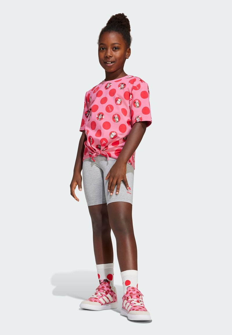 T-shirt rosa con grandi pois rossi e stampe di personaggi, abbinato a pantaloni corti grigi, calzature rosa e calze a fantasia.