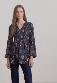 Marinblus med blommönster, volangkrage och trumpetärmar. Kombinerad med mörka jeans för en avslappnad look. Mjuk tyg med ett flödande design.