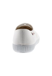 Sneaker bianco in tela con profilo basso, suola in gomma e dettagli cuciti. Presenta un'etichetta logo colorata sul tallone.