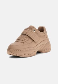 Grube beżowe sneakersy z grubą podeszwą, tłoczonym paskiem z logo na sznurówkach oraz subtelnym wzorem marki na górnej części.