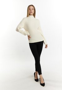 Geribbelde crème turtleneck trui met lange mouwen, gecombineerd met zwarte skinny broek en zwarte hoge hakken. Minimalistisch ontwerp.