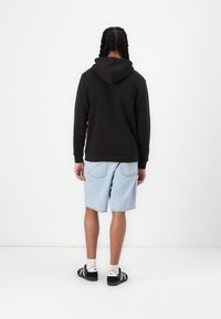 Felpa nera con cappuccio e tasca a marsupio, abbinata a pantaloni shorts in denim blu chiaro. Tessuto testurizzato, vestibilità comoda, indossata con sneakers nere.