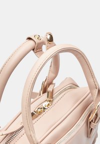 Borsa a mano in pelle beige con due manici, chiusure con zip e dettagli in hardware dorato. Texture liscia con cuciture lungo i bordi.