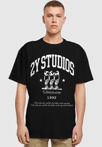 Čierne tričko s bielym grafickým textom "2Y STUDIOS Worldwide 1992" a tromi štylizovanými postavami držiacimi globy, s doplnkovým textom nižšie.