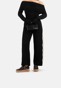 Top nero a spalle scoperte, pantaloni larghi neri con striscia laterale beige, abbinati a sneakers a fantasia marroni e una piccola borsa nera.