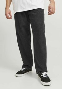 Pantalones de mezclilla negros con un corte relajado, que presentan una ligera textura de lavado y se combinan con zapatillas negras con cordones y suelas blancas.