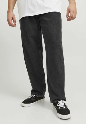 Pantaloni in denim nero con una vestibilità rilassata, caratterizzati da una leggera texture lavata e abbinati a sneaker nere con lacci e suole bianche.