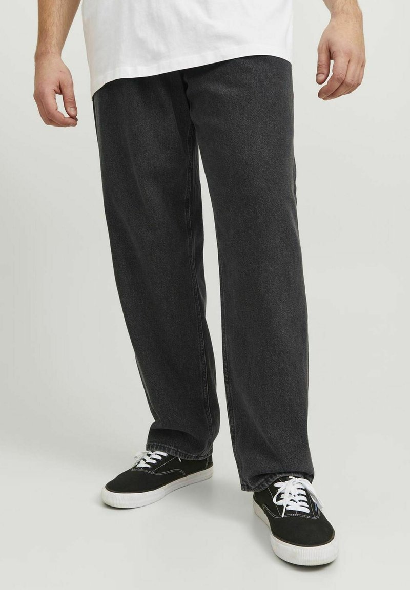 Pantaloni din denim negri cu un croi lejer, având o ușoară textură de spălare, asortați cu adidași negri cu șireturi și tălpi albe.