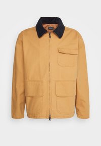Light brown jacket made of cotton, featuring a navy corduroy collar, zipper closure, and two front pockets with flap details.