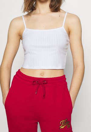 Hvid ribbet crop top med tynde stropper, der har en tætsiddende pasform og tekstureret stof. Kombineret med røde joggingbukser dekoreret med et logo.
