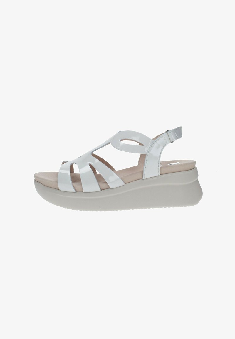 Sandalias de cuña de charol blanco con diseño recortado y correa de tobillo ajustable. Presentan una suela de plataforma texturizada en gris claro.